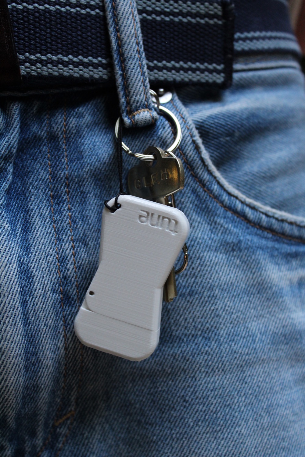The Tune Key hanging from a keychain on a belt loop, next to a house key