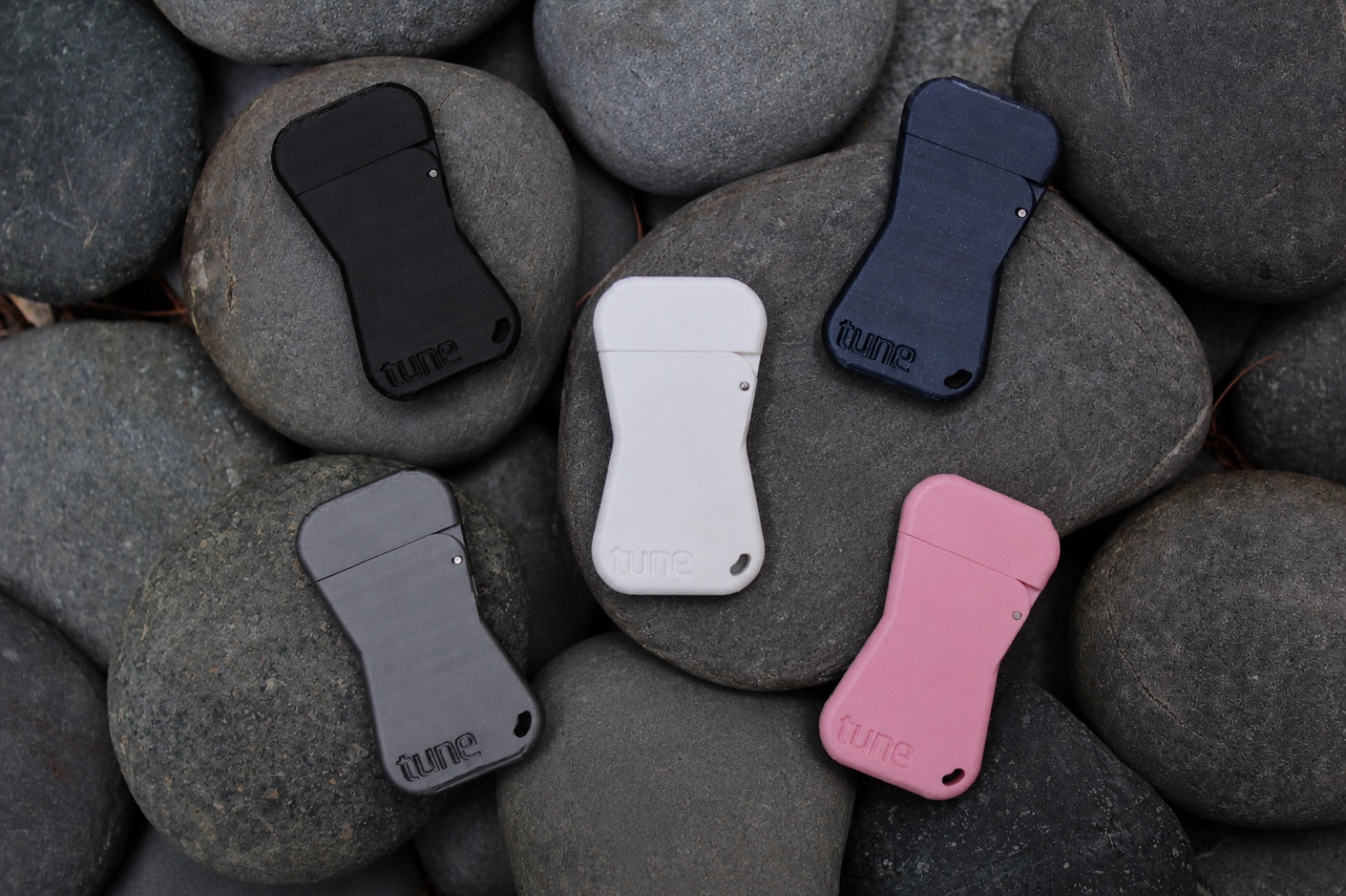 Five Tune Keys in black, navy, graphite, white, and pink resting on smooth stones